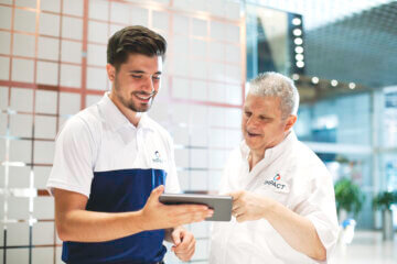 Two Impact employees, both wearing company shirts, look at information on a tablet together.