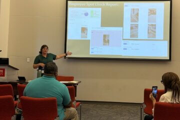 Kelly Freshcorn giving a presentation, with the slides showing screenshots of employee spot check inspections done in OrangeQC.