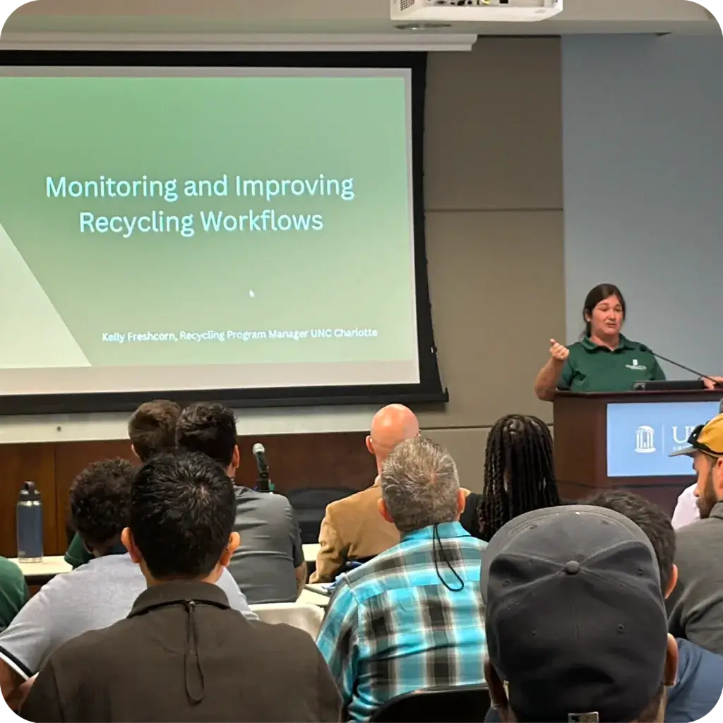 Speaker presenting a slide titled "Monitoring and Improving Recycling Workflows" to a seated audience in a conference room.